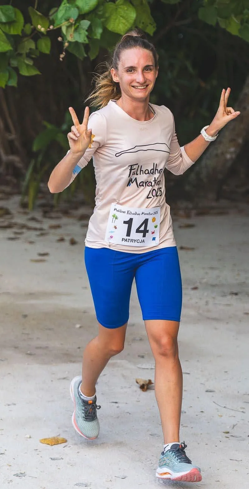 Patrycja podczas maratonu na Malediwach, z numerem startowym, w geście radości.